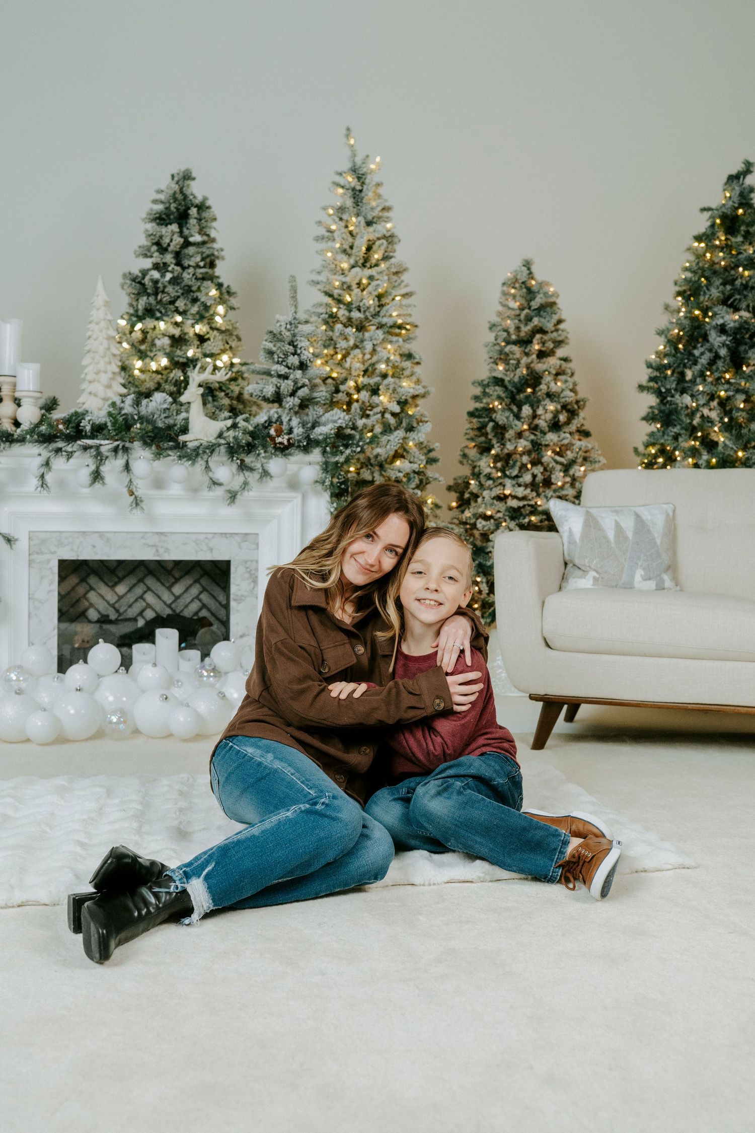 Holiday photo session with decorated Christmas trees, white furniture, and cozy winter setting on white carpet.
