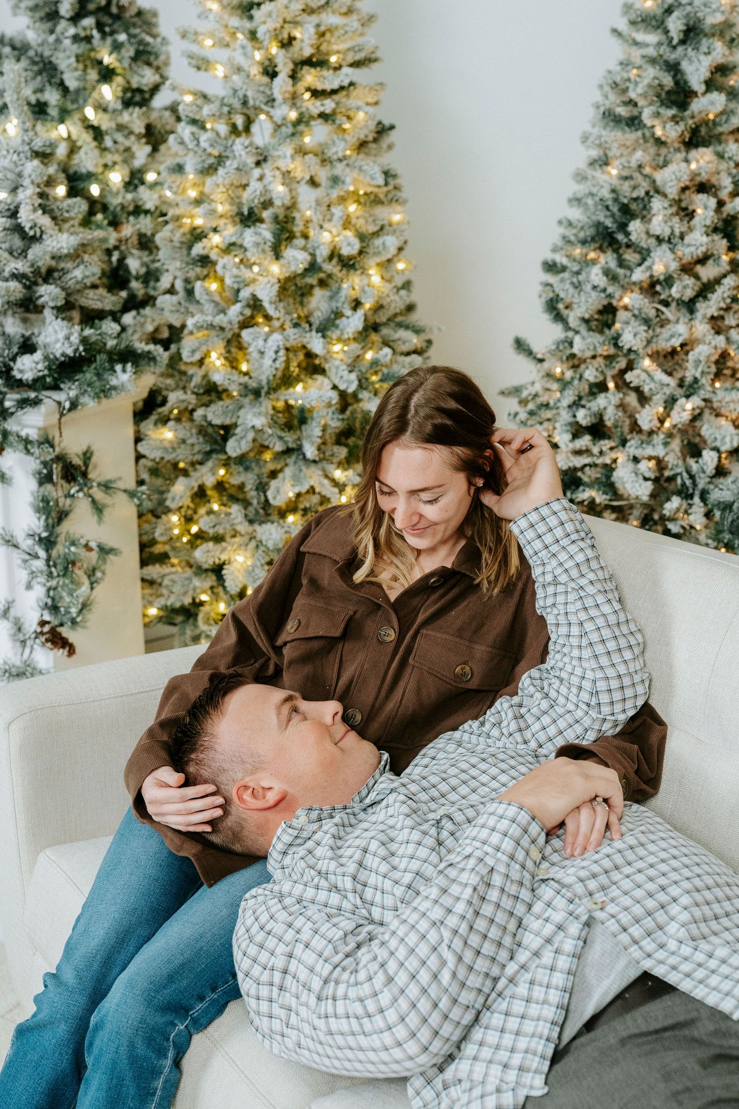 A couple shares joyful laughter while relaxing together near a decorated Christmas tree with white lights.
