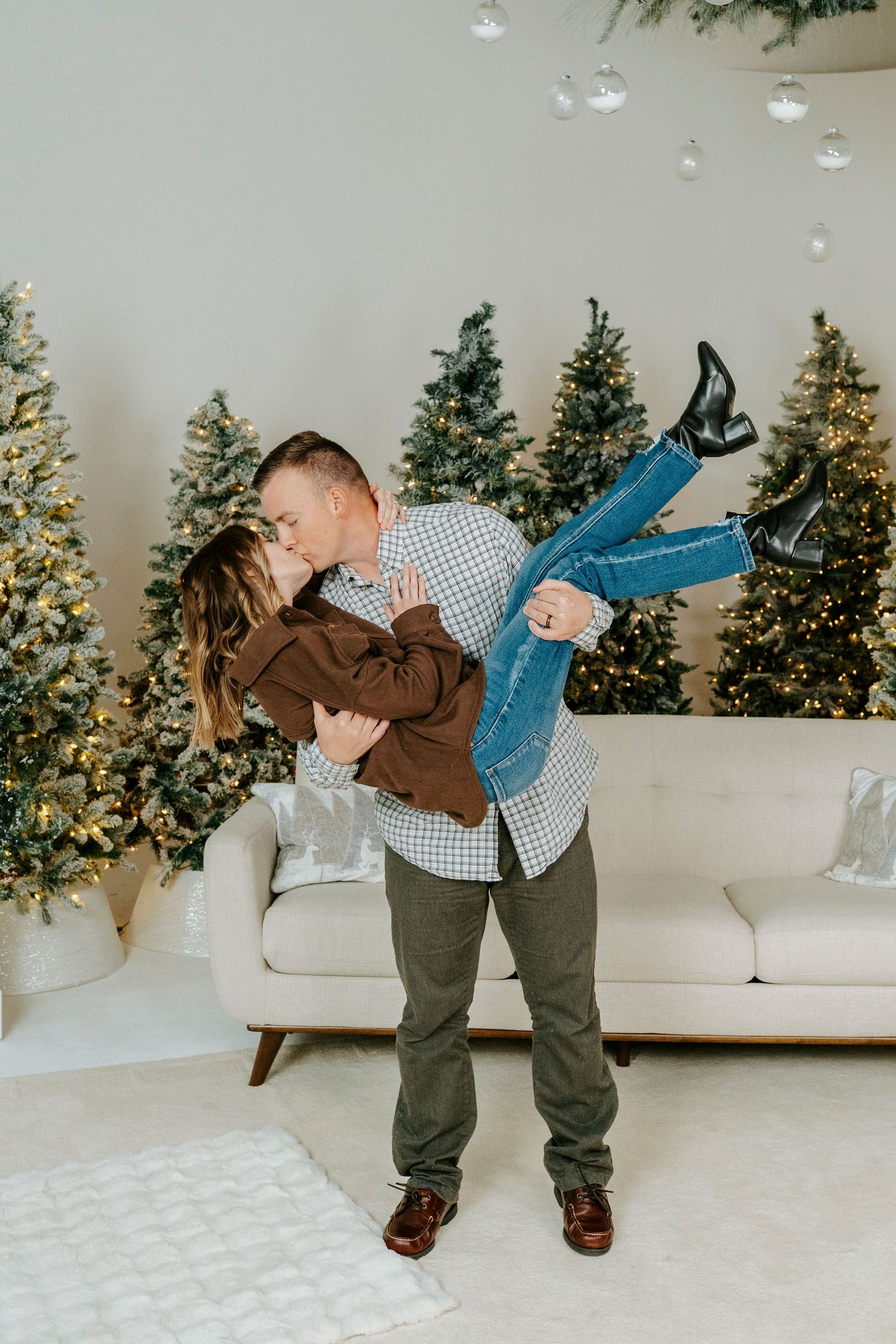A toddler in brown and blue clothing dances and spins in front of a white couch with Christmas trees in the background.