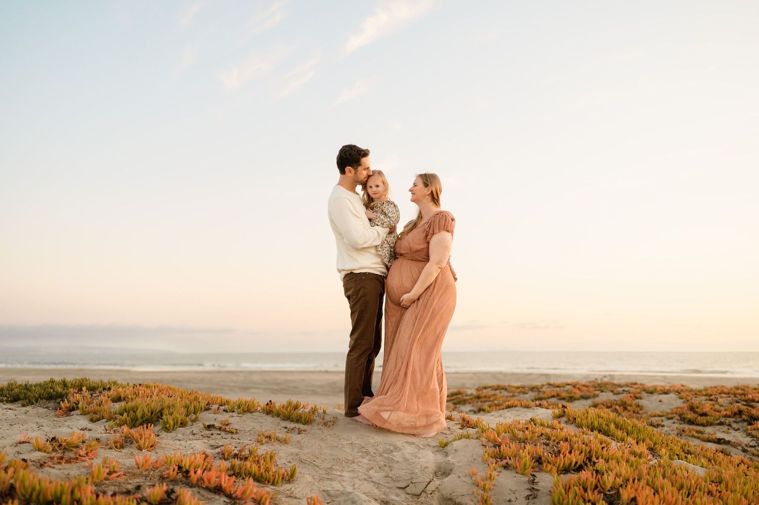 family stands on beach sand dunes during their Ventura beach maternity photoshoot while on babymoon, by Santa Barbara photographer