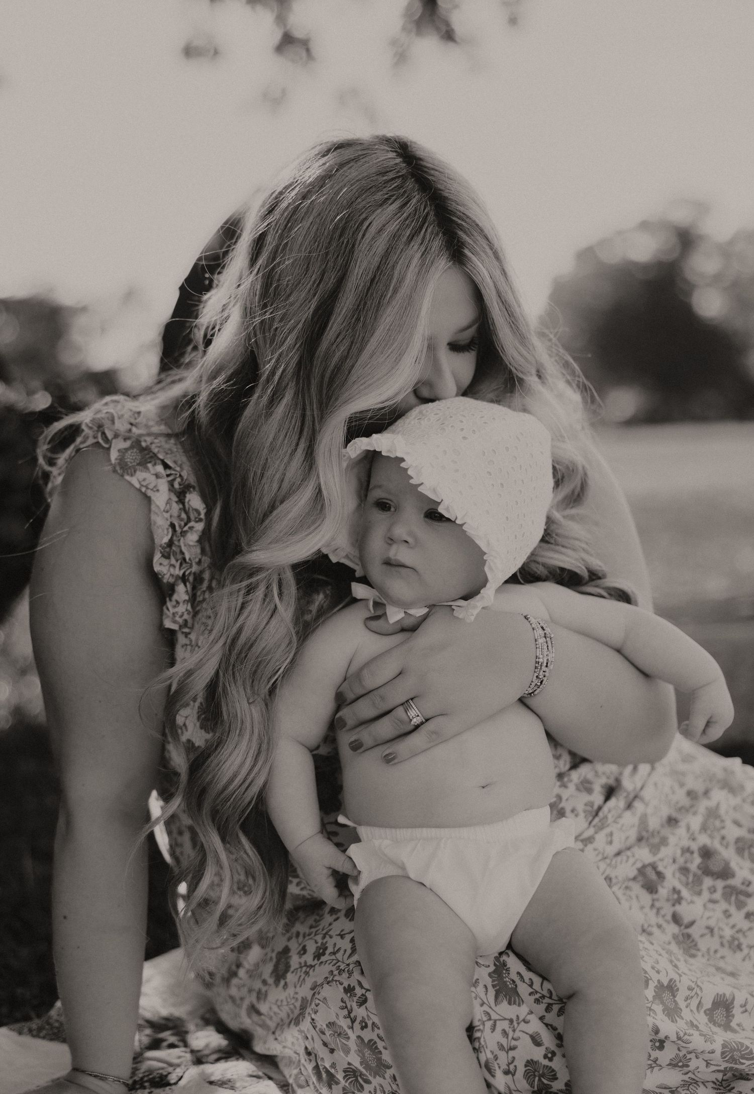 A tender black and white portrait of a mother and baby sharing an intimate moment on a blanket outdoors.