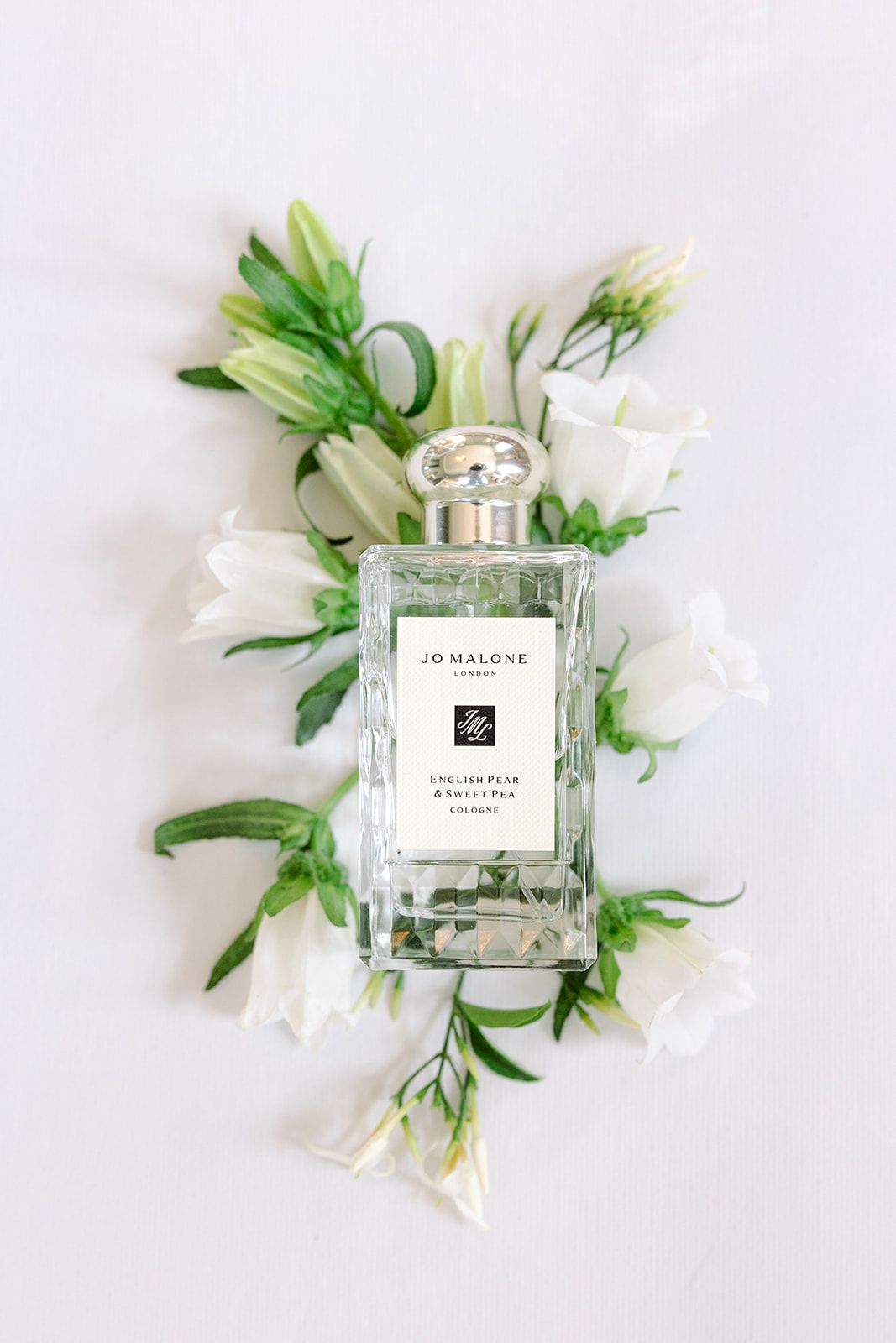 Jo Malone perfume bottle styled with white flowers and green leaves on white background in multiple angles.