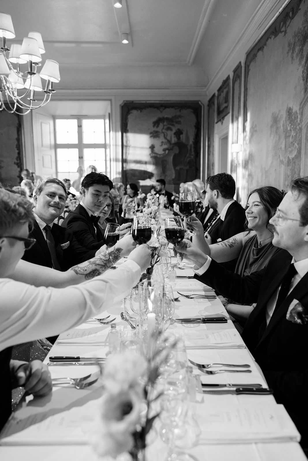 Black and white photo series showing a lively dinner party with guests seated at a long table raising glasses in celebration.