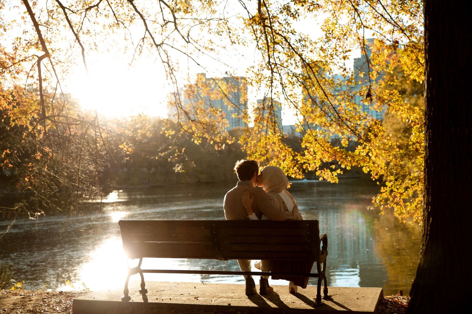 A serene sunset moment on a park bench overlooking a lake with golden autumn foliage.