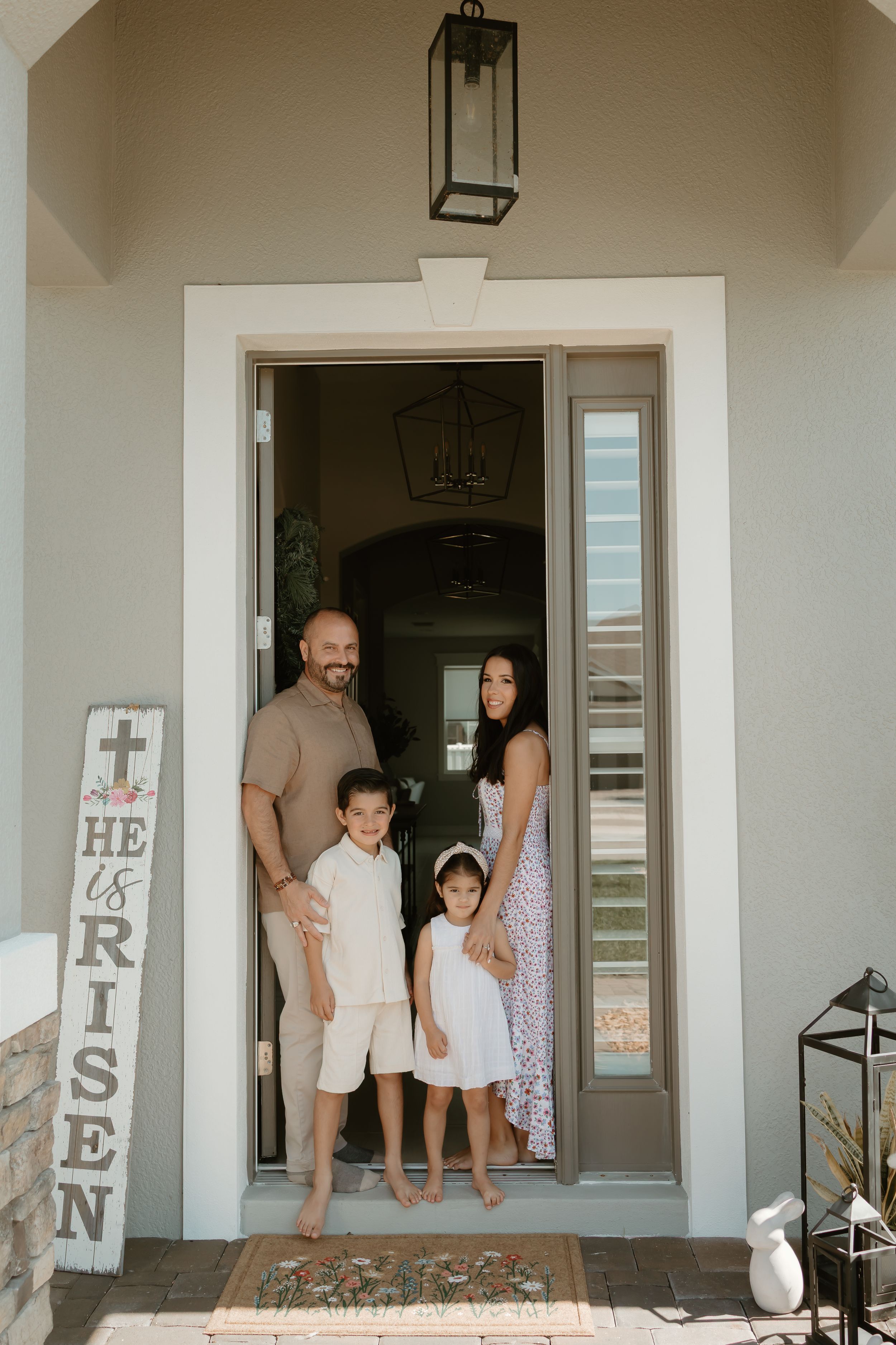 Family stands in doorway of modern white house with decorative signs.