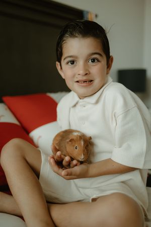 Child in white shirt holding small brown hamster on red couch.