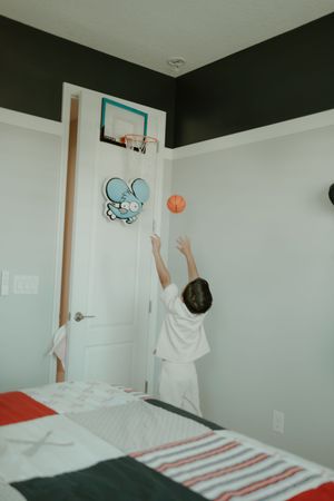 A small basketball hoop mounted on a white door in a bedroom with black and white walls.