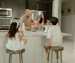 A modern white kitchen with family gathered around counter stools.