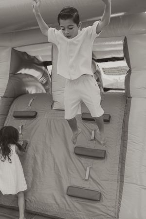 Children playing and jumping on a gray mattress in a sequence of action shots.