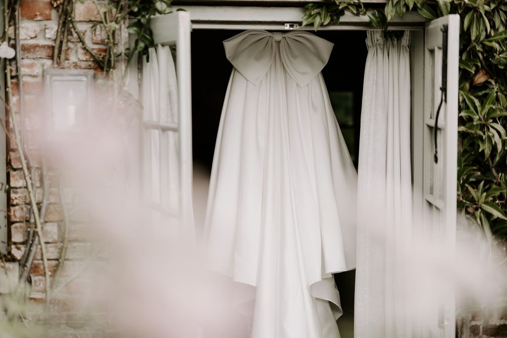 A white wedding dress hangs elegantly in a doorway with flowing fabric and veil against a rustic backdrop.