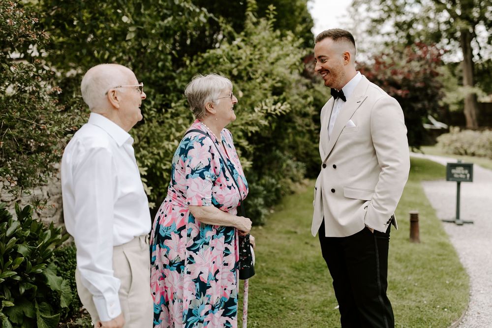 Wedding guests share joyful moments in a garden setting wearing formal attire and floral prints.