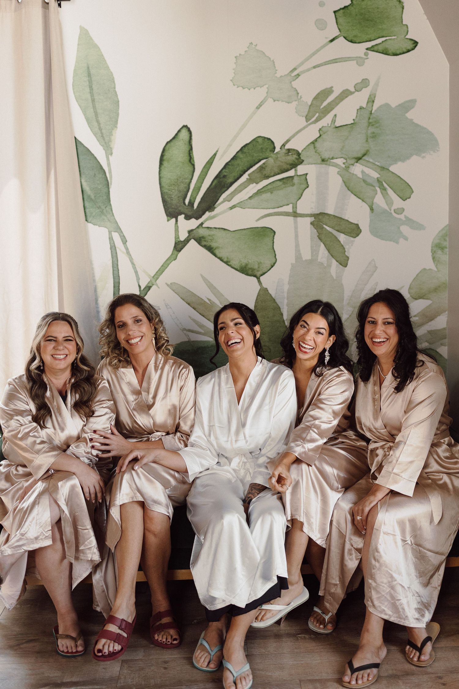 Wedding party in silk robes sitting together against a botanical wall mural.