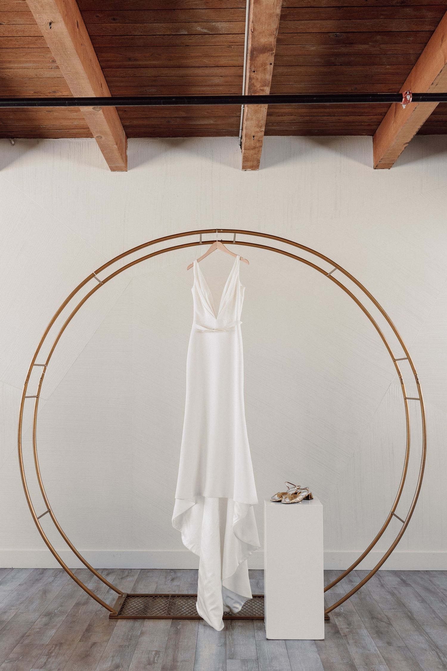 White wedding dress hanging on a circular copper arch against a white wall.