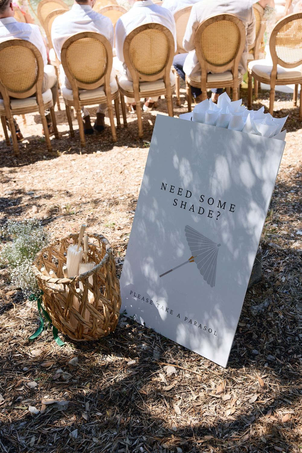 Wedding ceremony chairs with signs reading 'Need Some Shade' in a sunny outdoor setting.