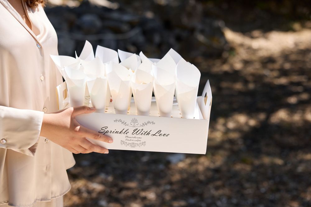 Hands holding a wooden box filled with white paper wrapped sparklers for a wedding celebration.