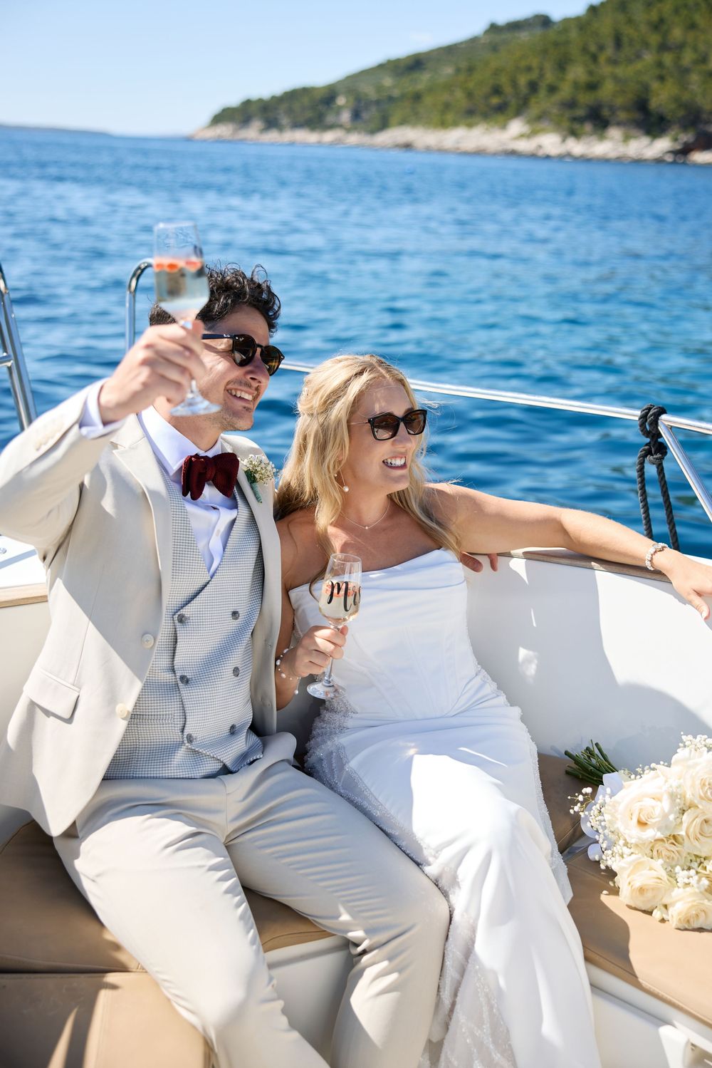 Wedding party relaxing on a luxury yacht with coastal scenery in the background.
