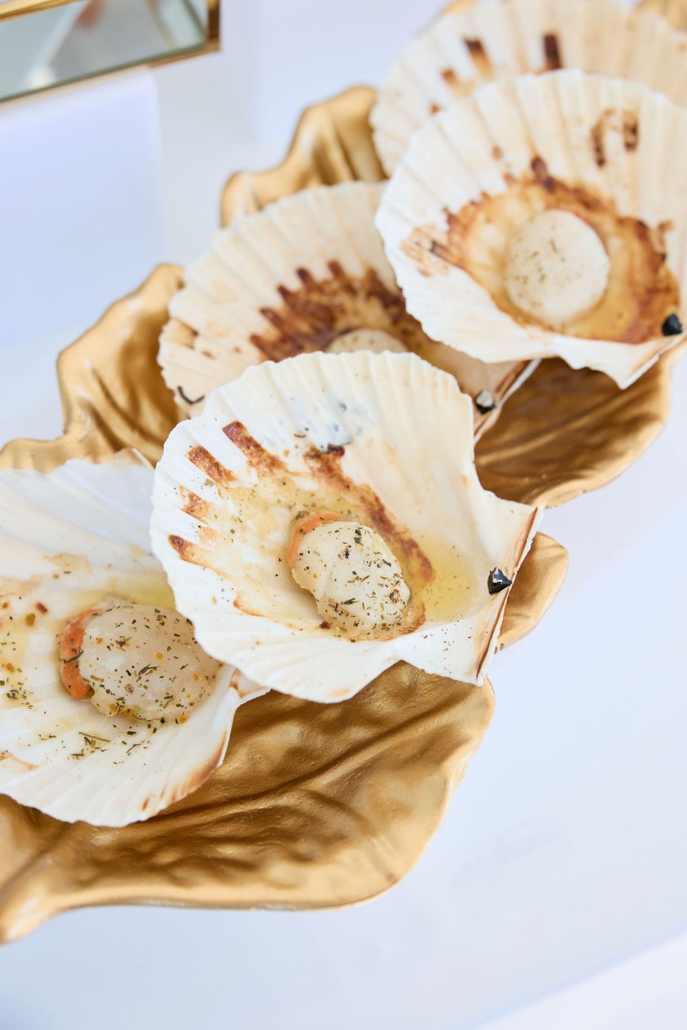 Seared scallops served in elegant white scallop shells arranged on golden paper.