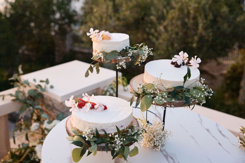 A white linen tablecloth adorned with delicate floral arrangements and scattered petals creates an elegant outdoor setting.