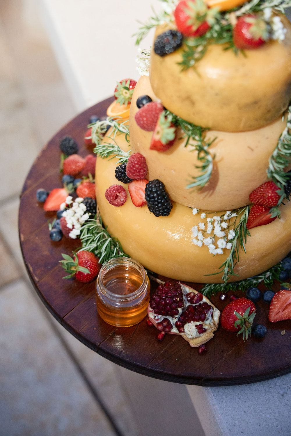 Golden wedding cake decorated with fresh berries and greenery on a wooden board.