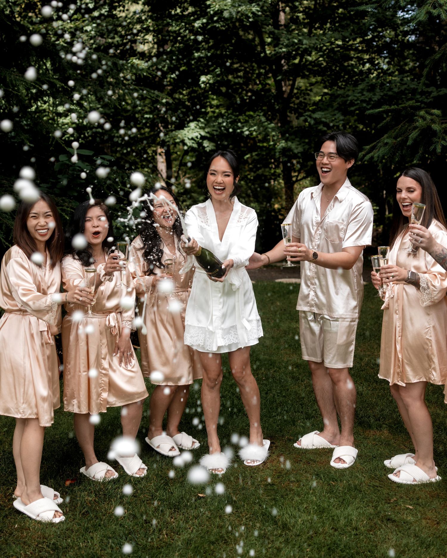 Wedding party members in matching silk robes pose playfully on grass for a group photo.
