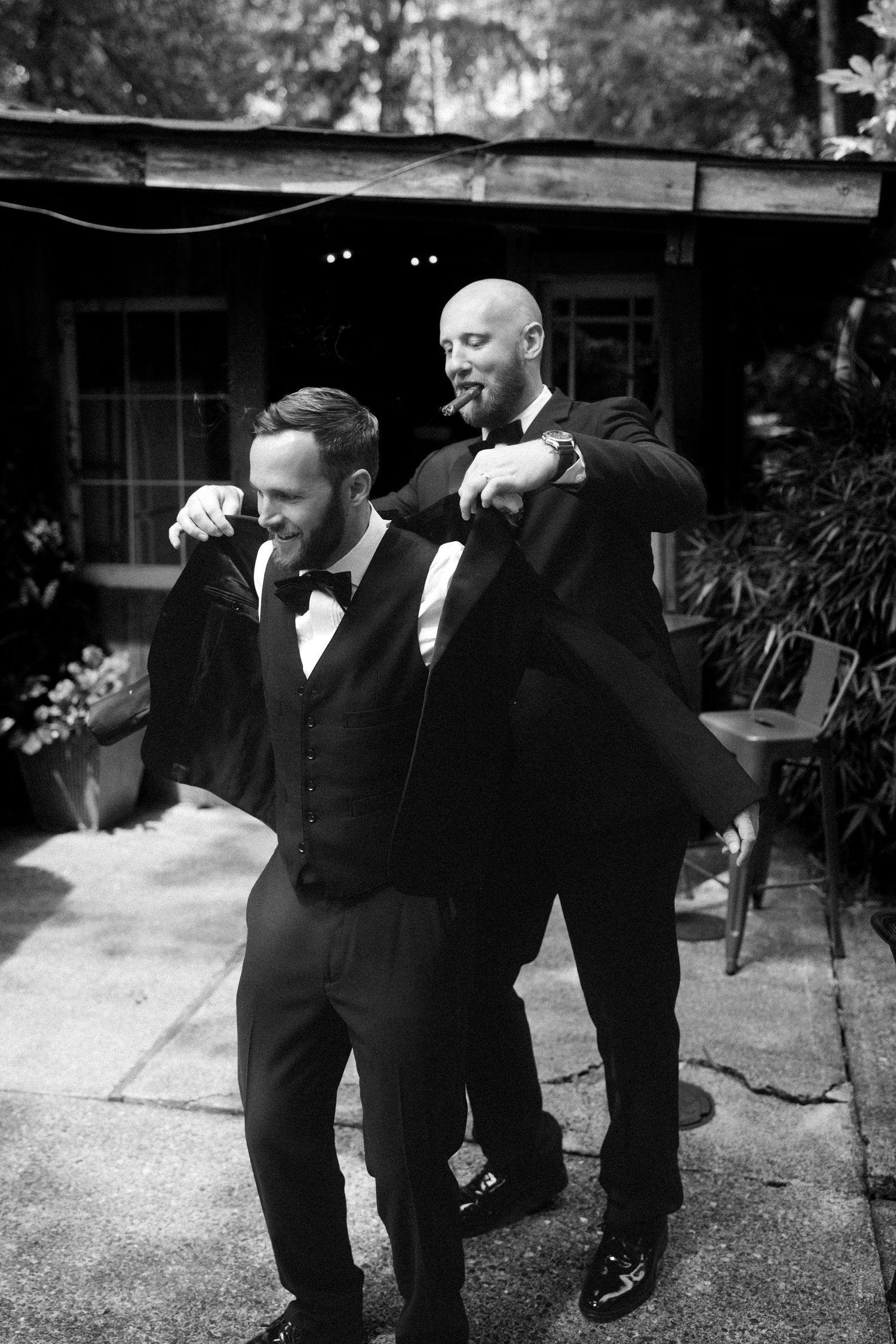 Groomsmen in black tuxedos strike fun poses together during wedding photo session.