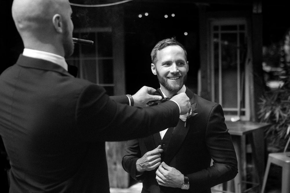 Men in formal black suits gather in a dimly lit room during an elegant event.