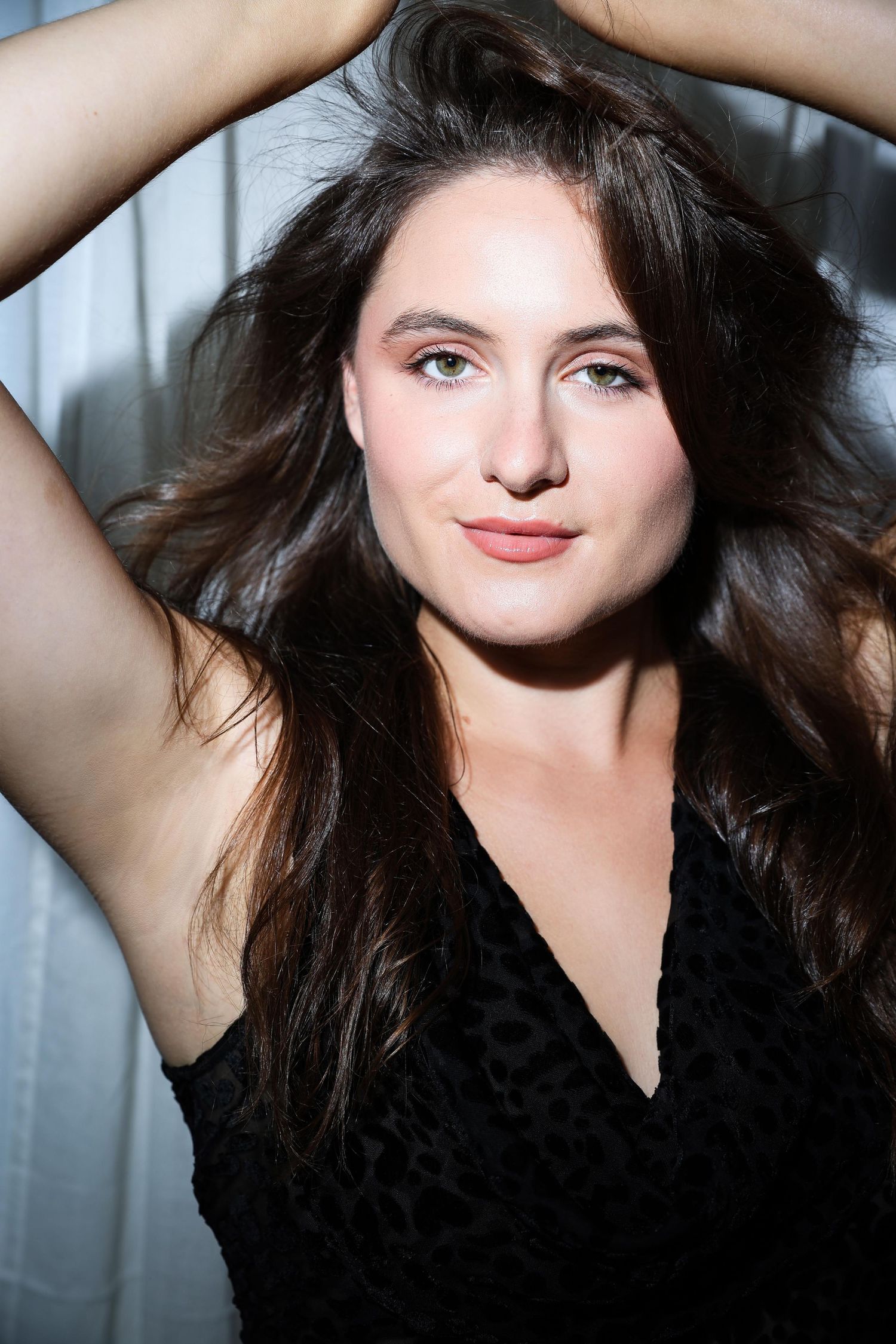 Four close-up portraits of a woman with dark wavy hair posing with raised arms against a light background.