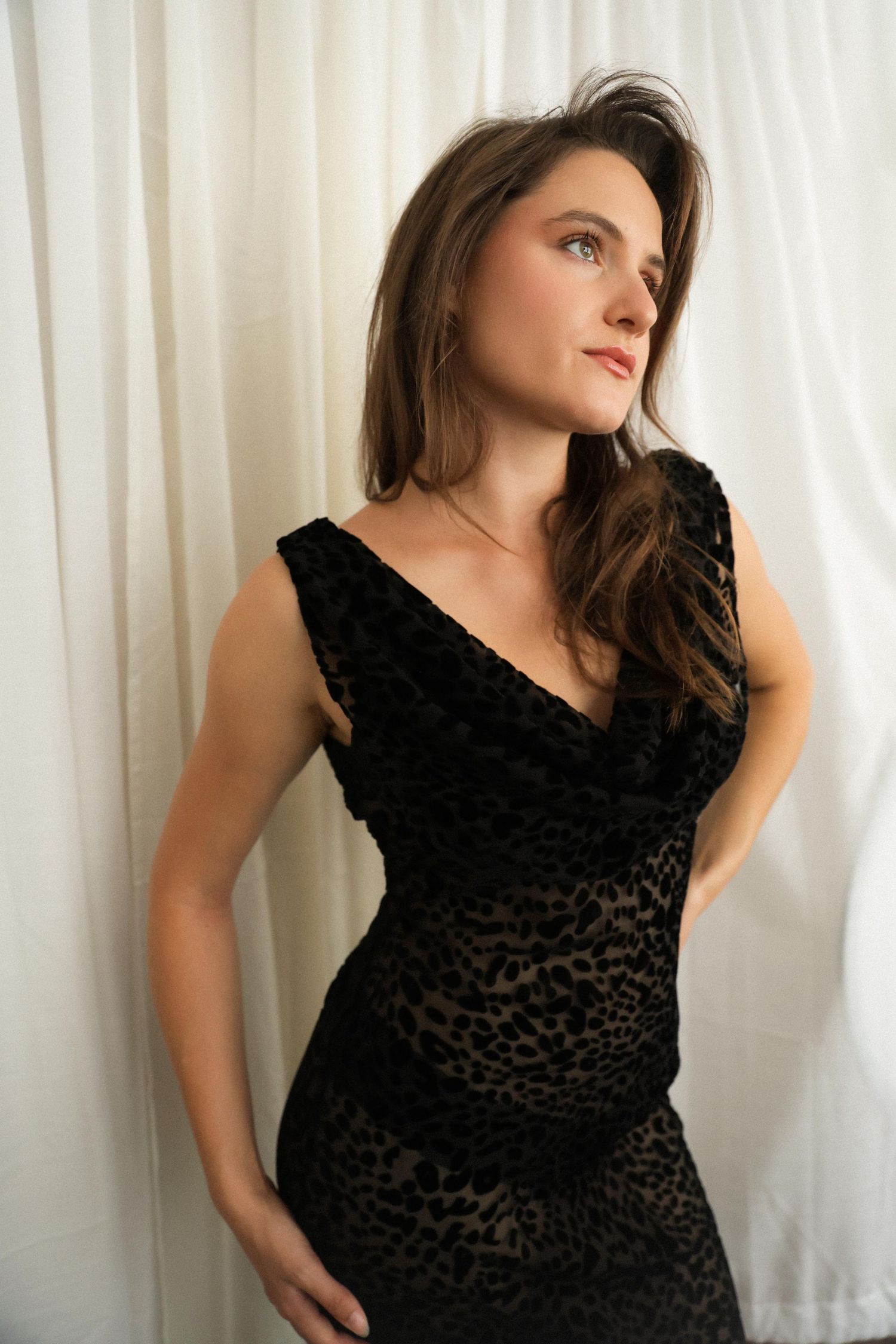 A woman in a black velvet dress poses against a white curtain backdrop in a series of artistic portrait shots.