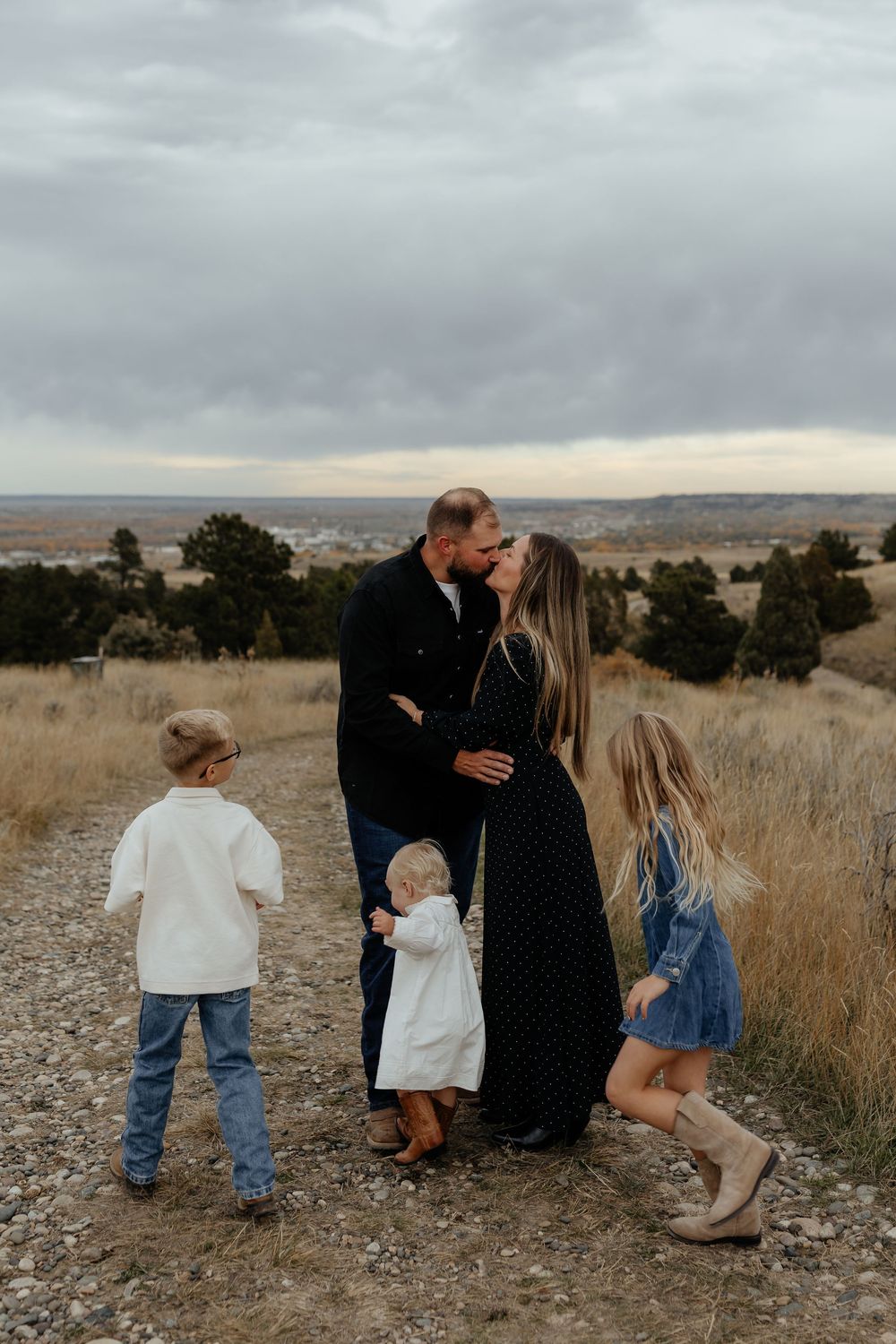 Family walking together through a scenic field of tall grass at sunset with mountains in the background.
