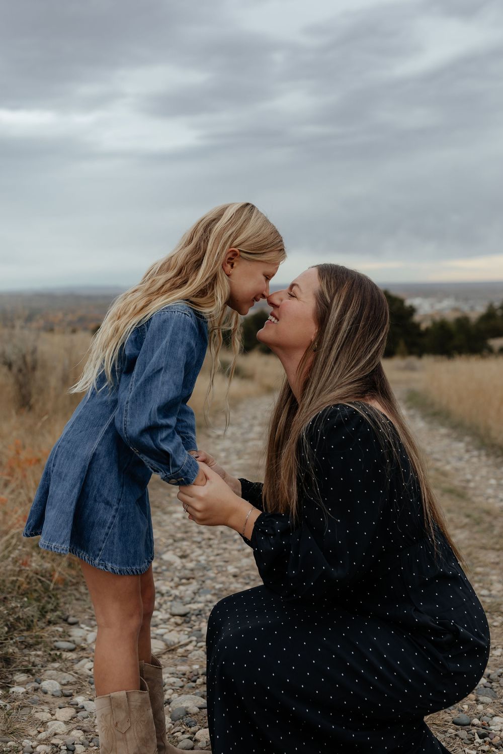 A tender moment between parent and child sharing kisses outdoors on a cloudy day in a rustic field setting.