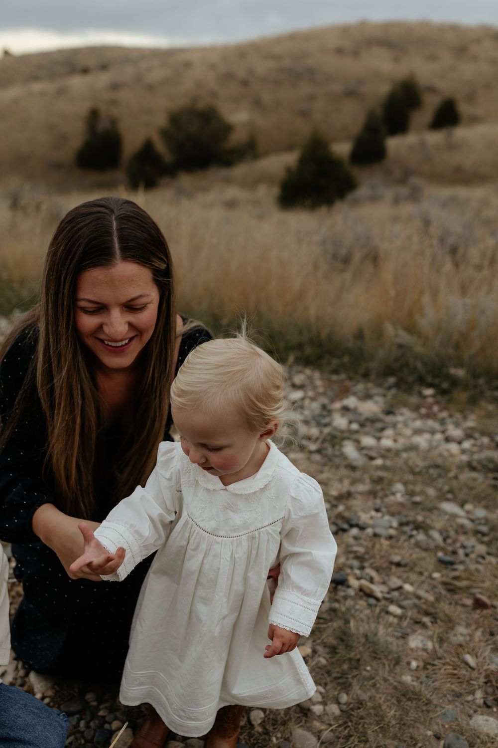 A tender outdoor photoshoot in a grassy field shows joyful moments between a parent and child in white dress.