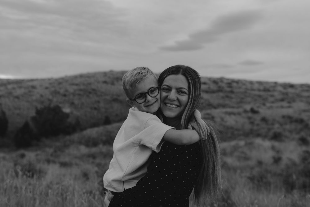 Two people embrace warmly while standing in a scenic mountainous landscape at sunset.