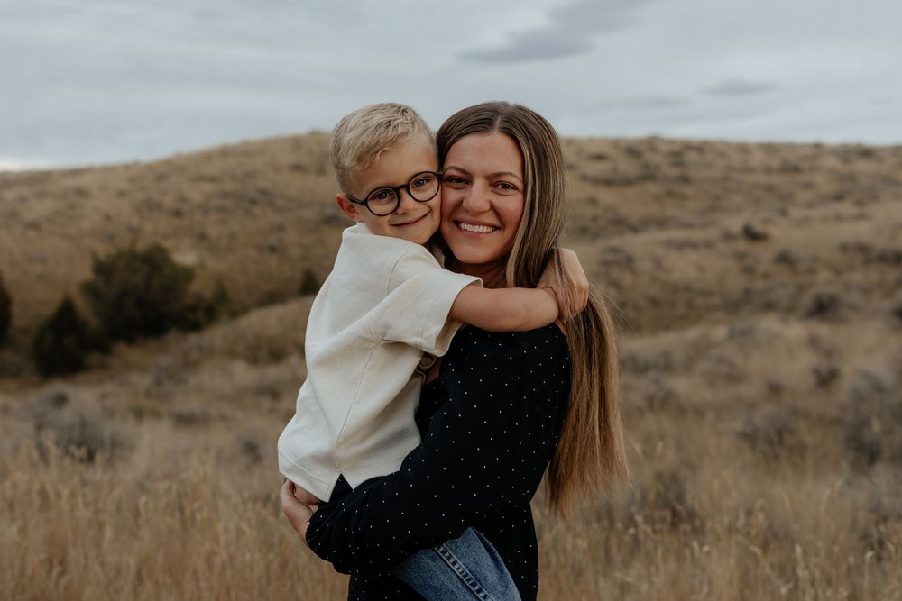A warm embrace shared between two people on a golden hillside during sunset with dry grass and rolling hills in the background.