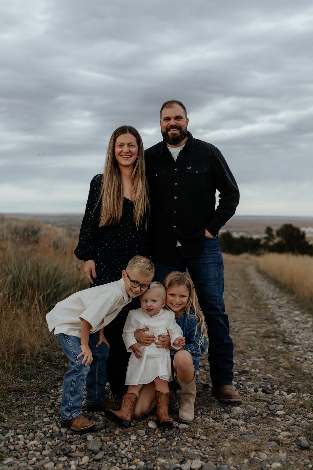 Family portrait series on a rocky path showing candid moments of parents and children against cloudy sky.