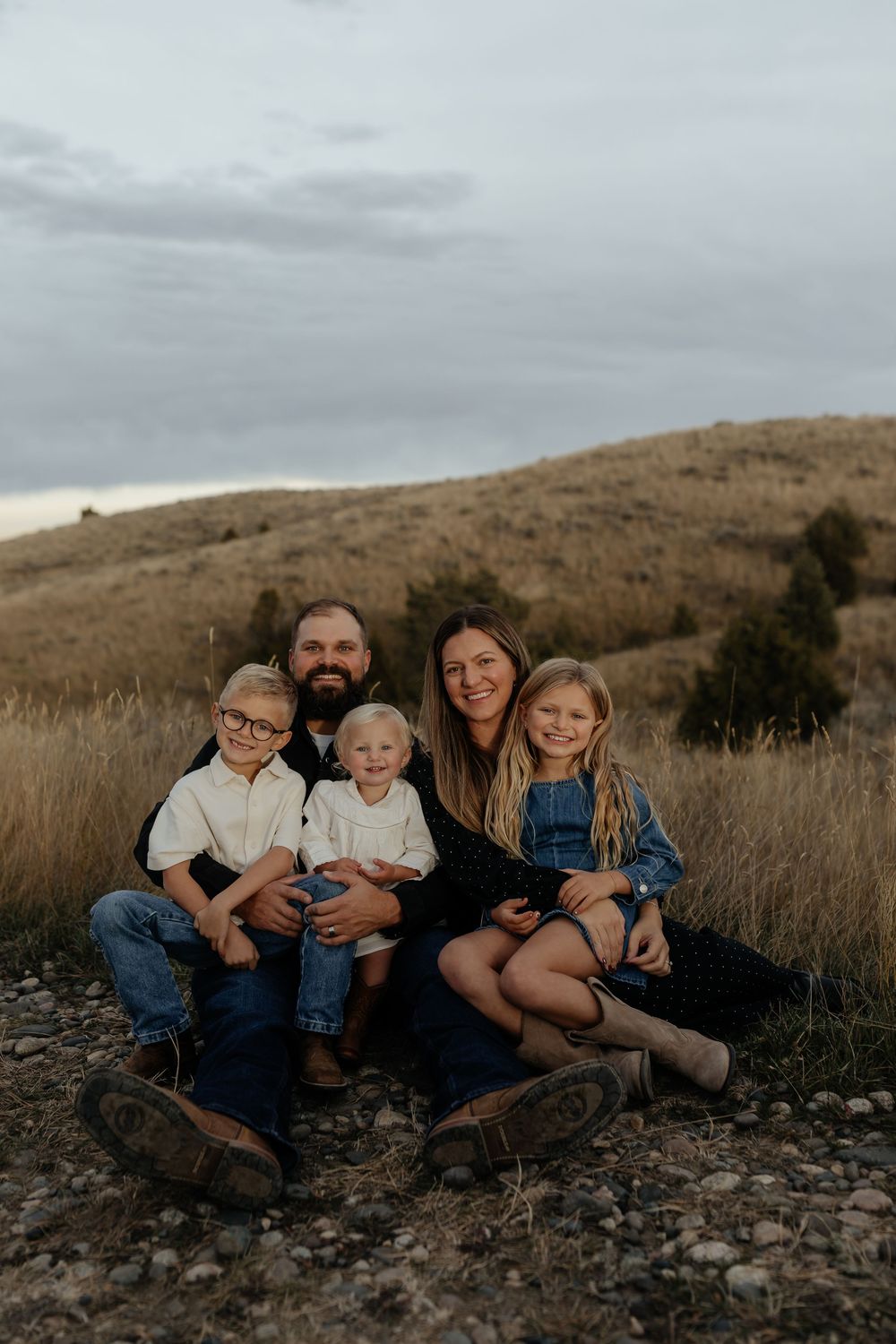 A family sits together on rocky ground against a backdrop of rolling hills during golden hour.