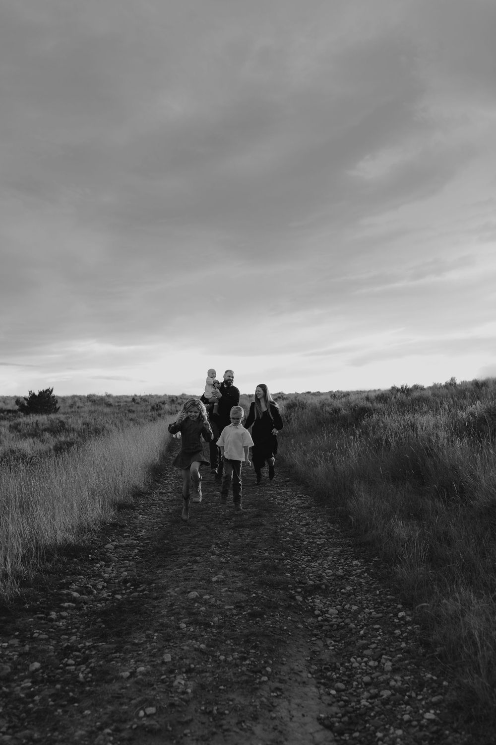 A group walking together on a dirt path through grassy fields under cloudy skies in black and white.