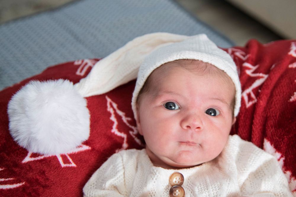 Adorable newborn baby in white knit outfit and bunny ear hat lying on a red Christmas blanket.