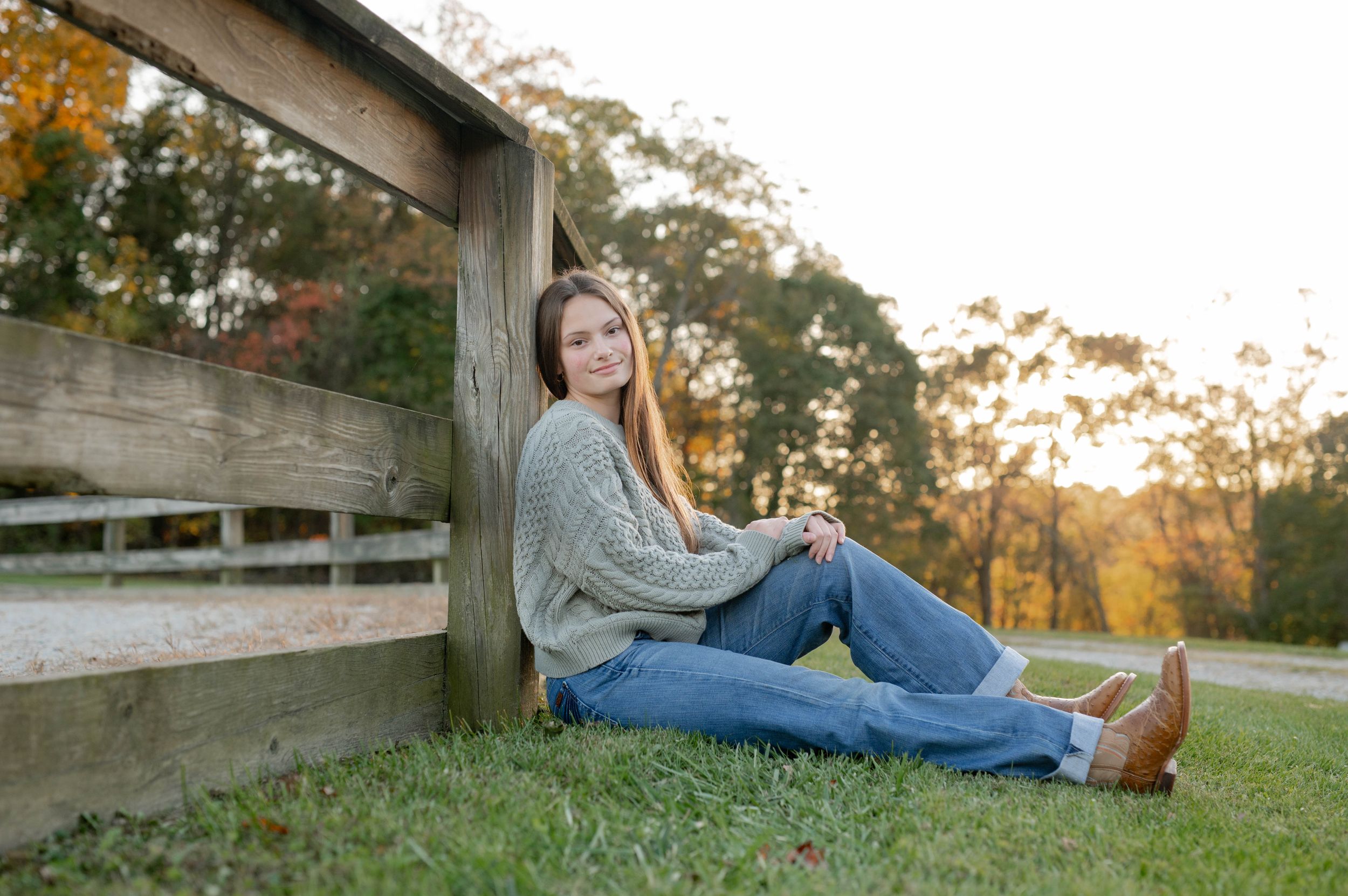 A casual autumn portrait on a wooden fence with boots and jeans at golden hour sunset.