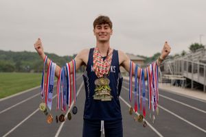 Athlete displays collection of medals on running track with bleachers in background.