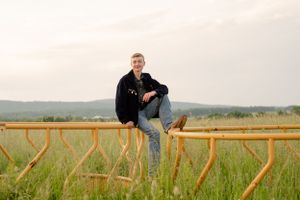 Senior portrait of person balanced on wooden fence in rural field at sunset.