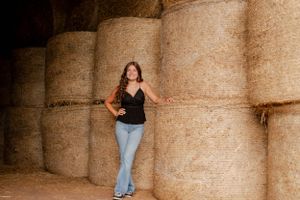 Person in casual attire posing against stacked hay bales in warm lighting.