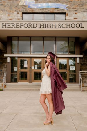 Graduate in maroon cap and gown poses outside Hereford High School entrance.