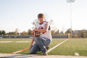 Football player kneeling with ball on field with stadium lights in background.