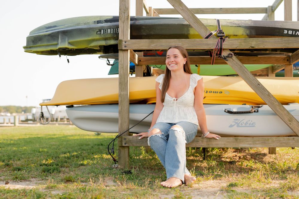 Sitting beneath stacked kayaks and canoes on outdoor storage rack.