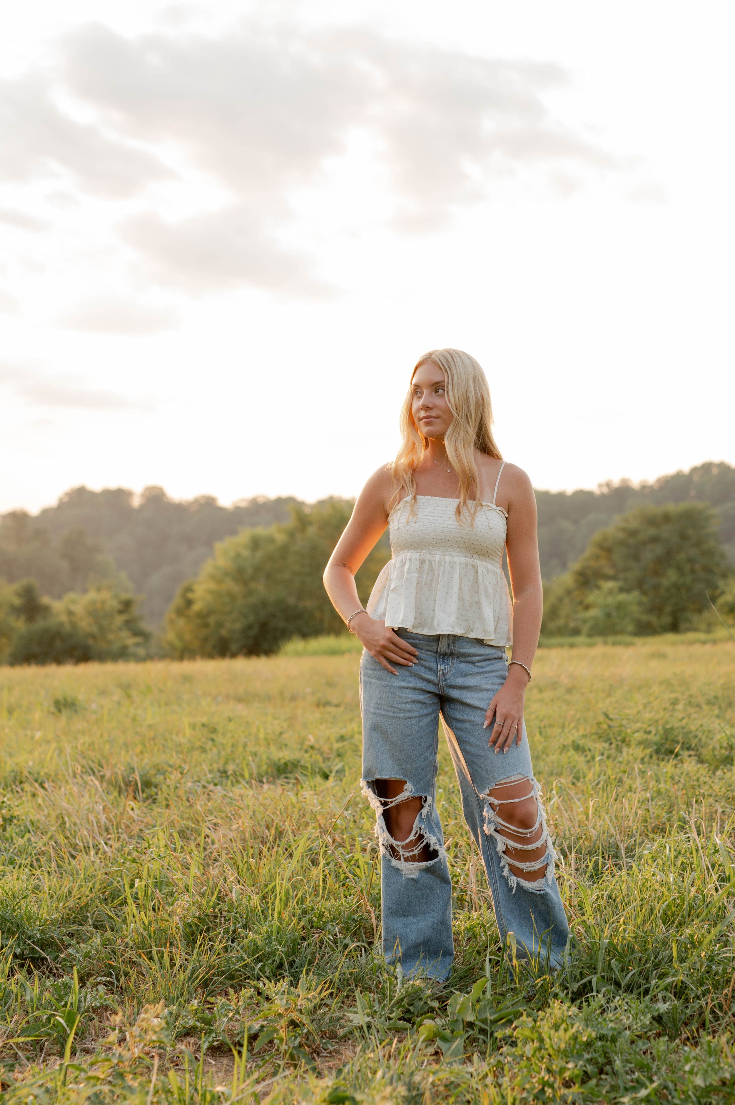 Person wearing ripped jeans and white top standing in golden sunlit meadow.