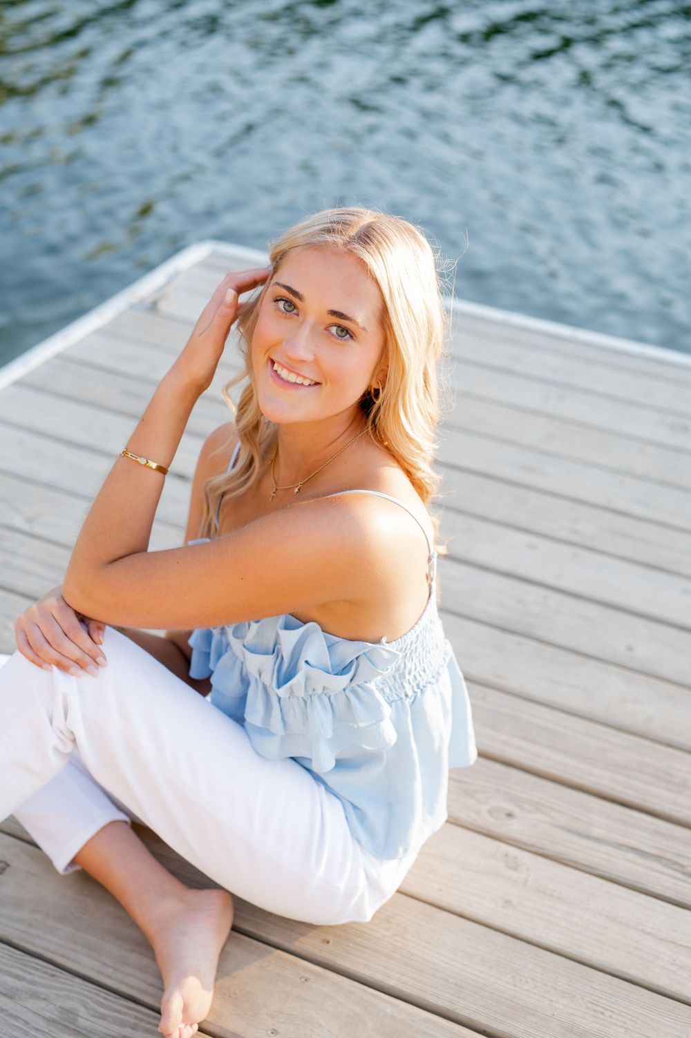 Summer portrait on a dock with light blue off-shoulder top and white pants.