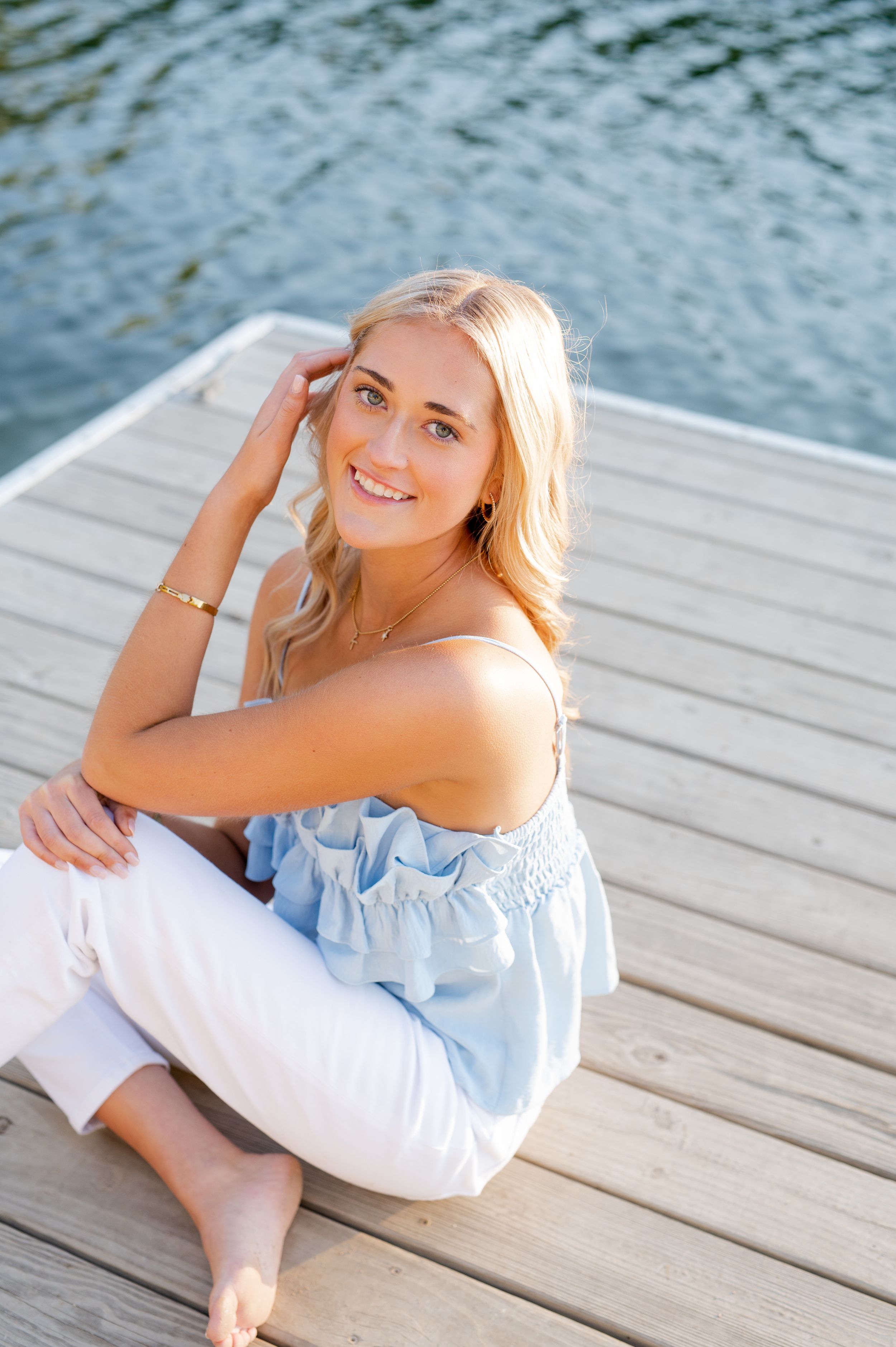 Summer portrait on a dock with light blue off-shoulder top and white pants.