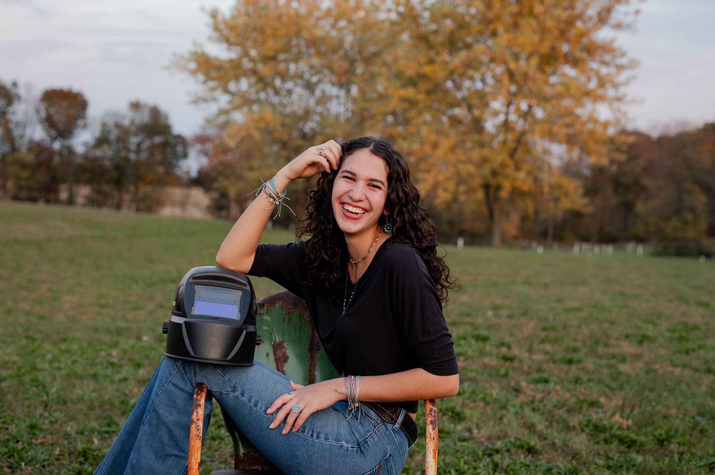 Casual autumn portrait sitting on farm equipment in a field with fall foliage.