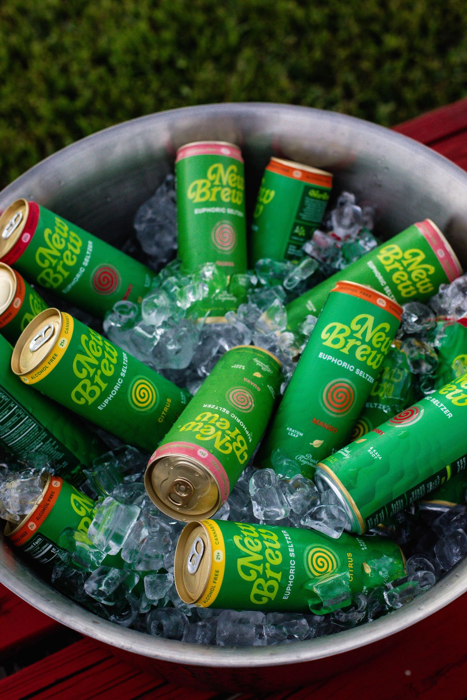 Metal bowl filled with iced New Brew canned beverages on wooden surface.