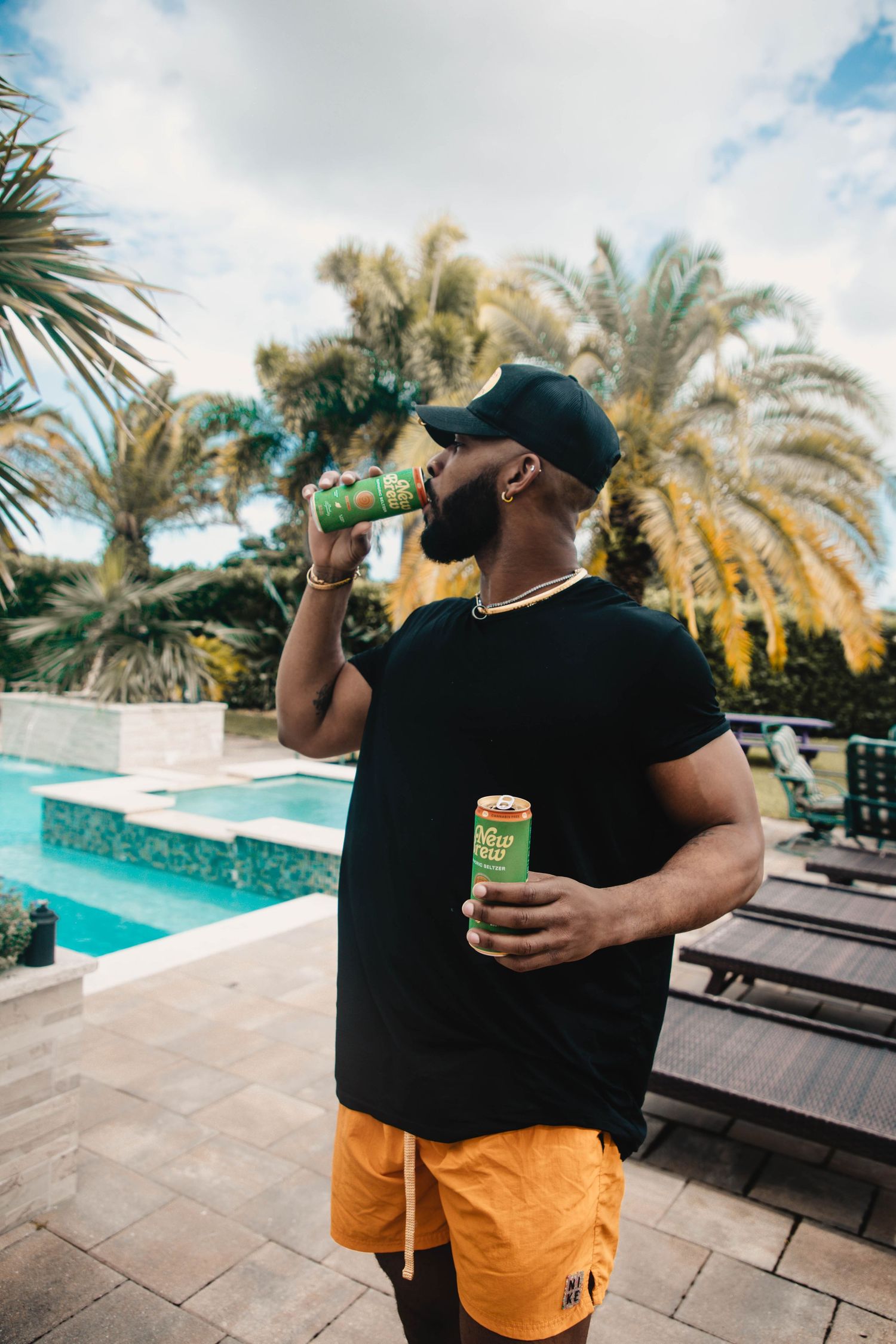 Person enjoying New Brew drinks by luxurious pool with palm trees.